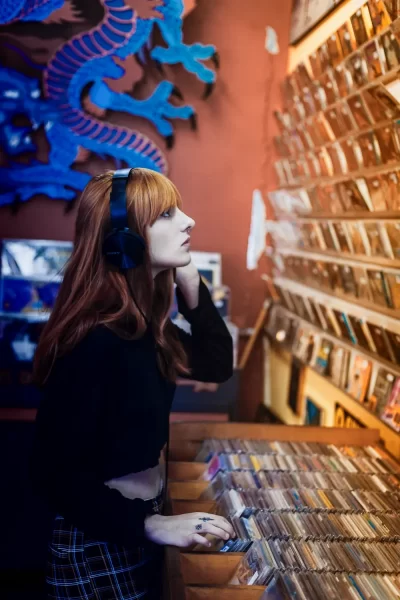 chica escuchando un CD y mirando una pared llena de discos de CD