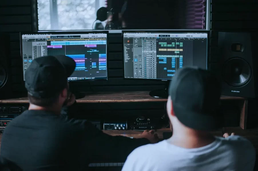 dos chicos delante de dos monitores creando su propia música en su estudio de grabación